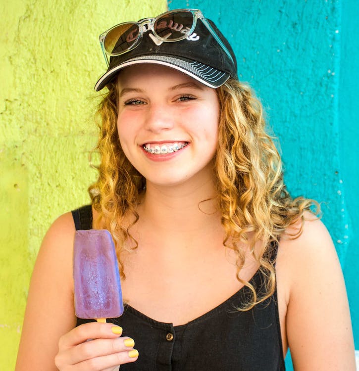 A girl with braces is smiling while holding a popsicle.