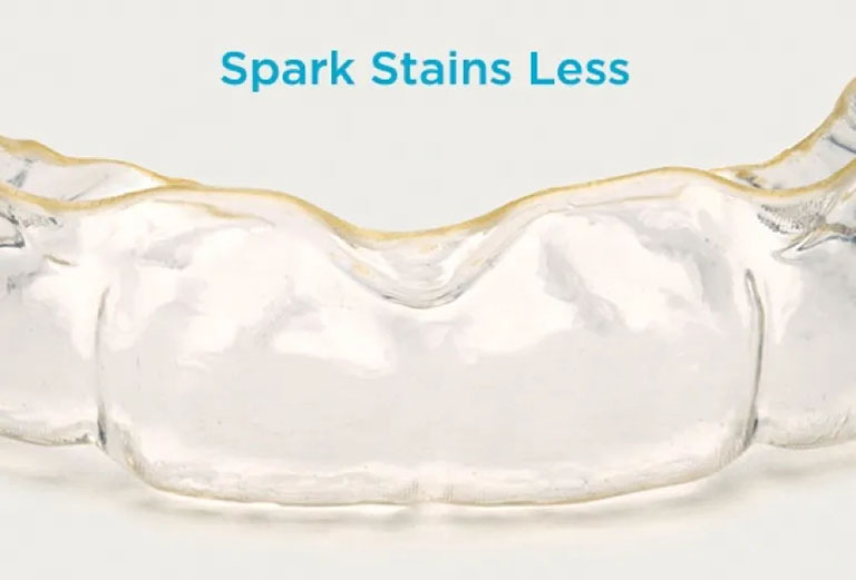 Pictured is a Spark Clear Aligner. Blue text above reads "Spark Stains Less"