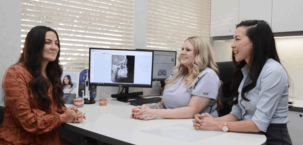 A patient is sitting at a desk speaking with a treatment coordinator and Dr. Kat at a free consultation